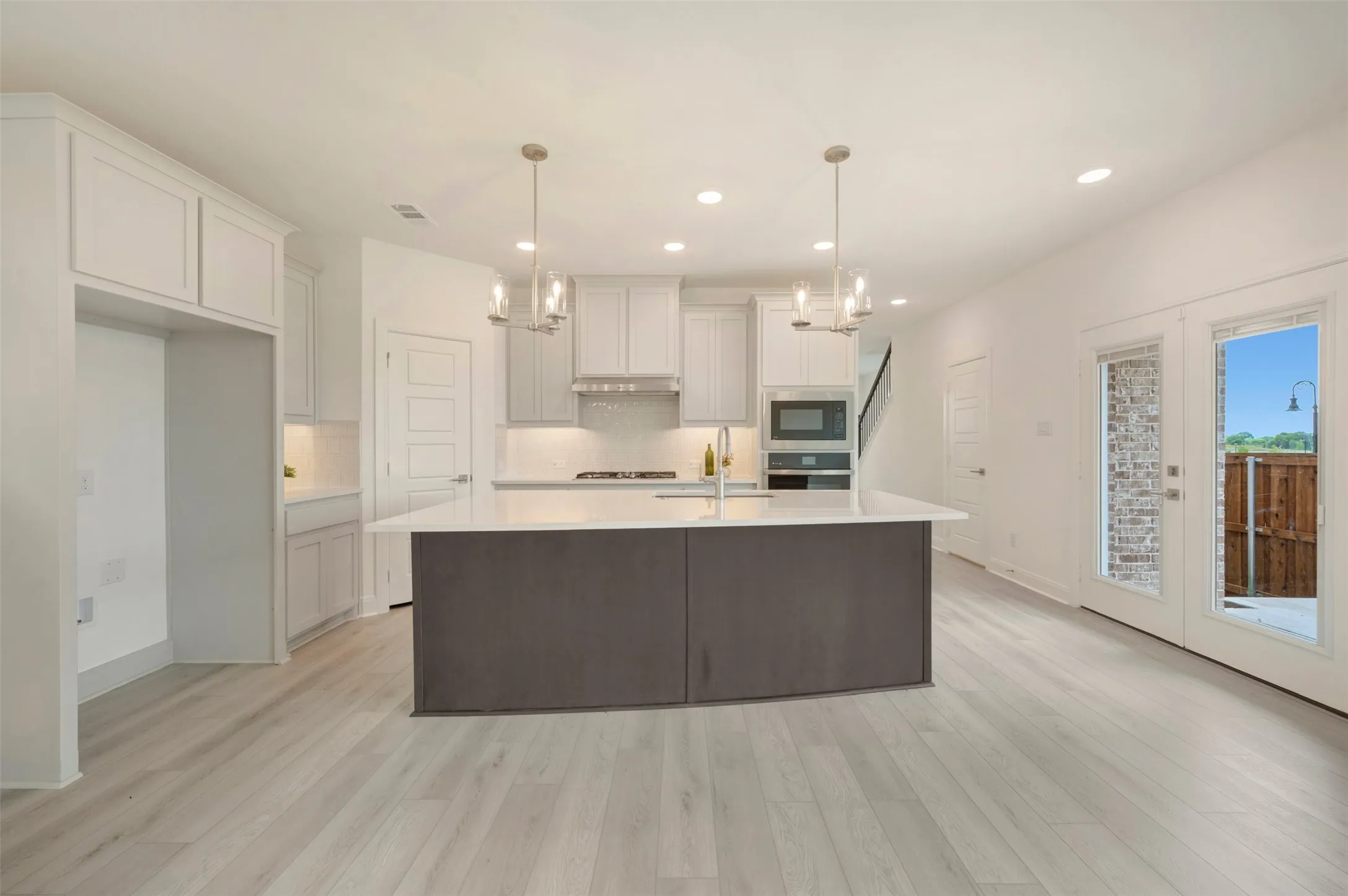 Open-concept kitchen featuring a large central island with seating, pendant lighting, built-in microwave, and wood-finish flooring