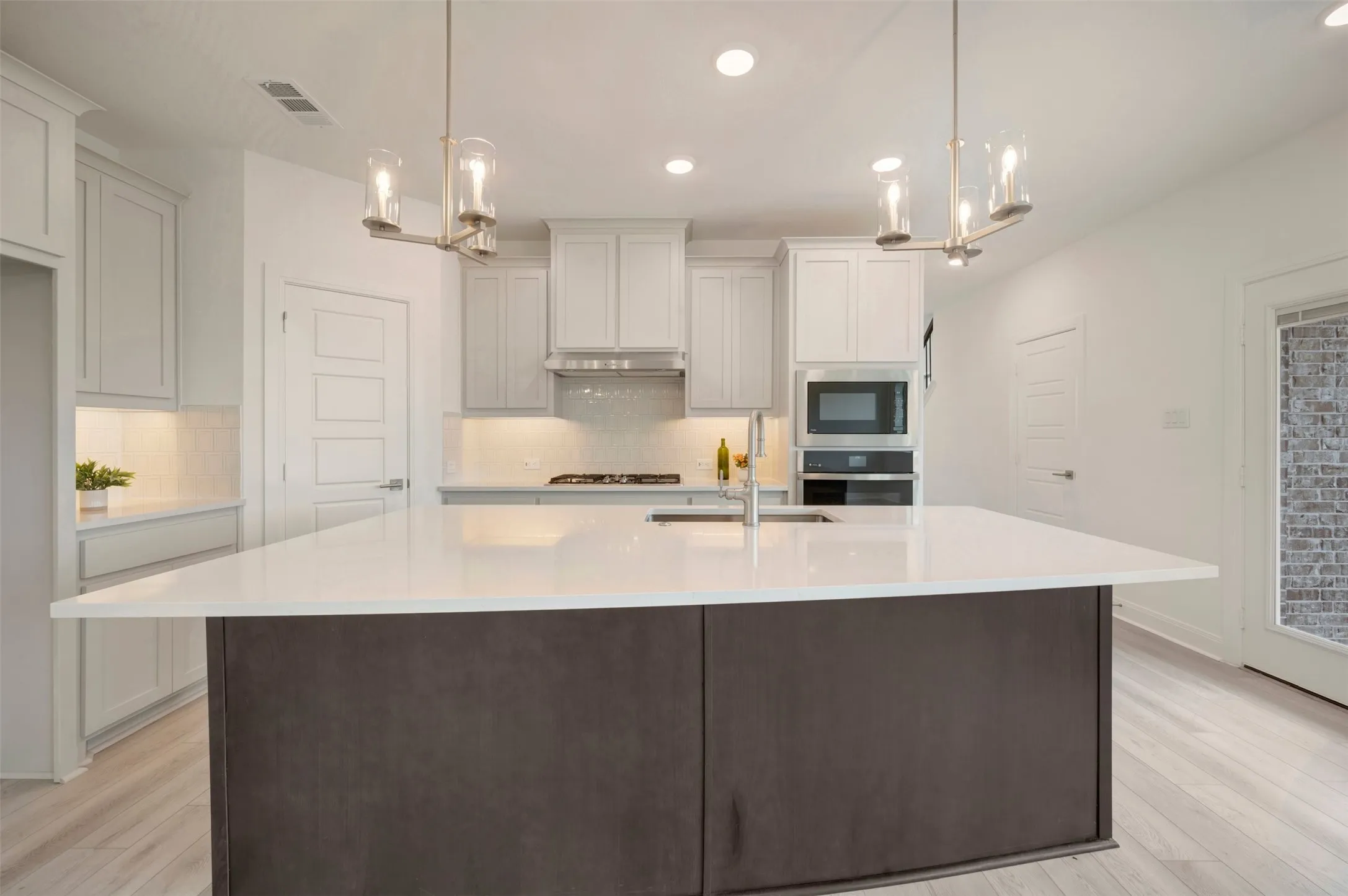 Kitchen featuring a dark-toned island with a white countertop, stainless steel appliances, white cabinetry with under-cabinet lighting, and light wood-finish flooring