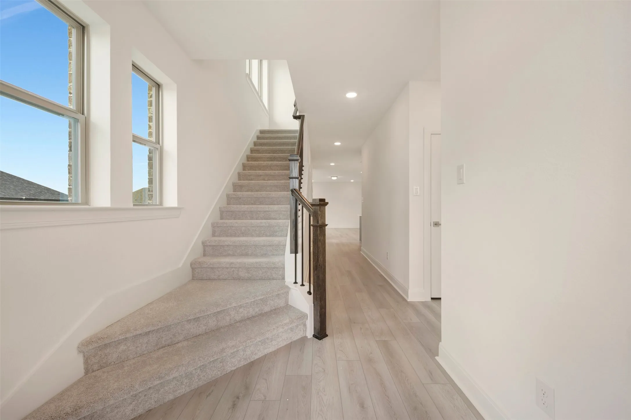 Staircase with carpeted treads and risers, featuring a dark wood-finish handrail and black metal balusters