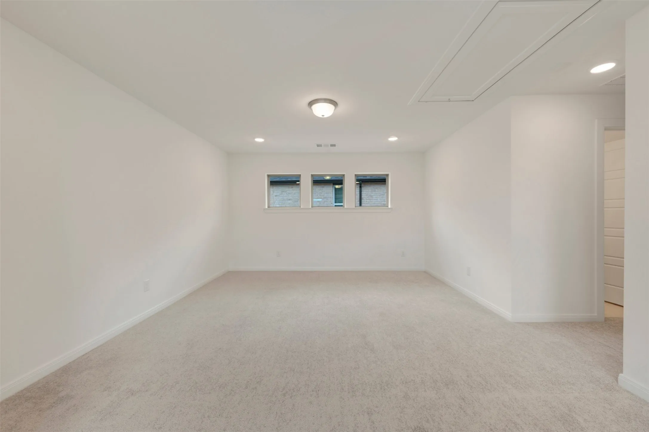 Carpeted room featuring recessed lighting, a central flush-mount fixture, three horizontal windows, and white baseboards