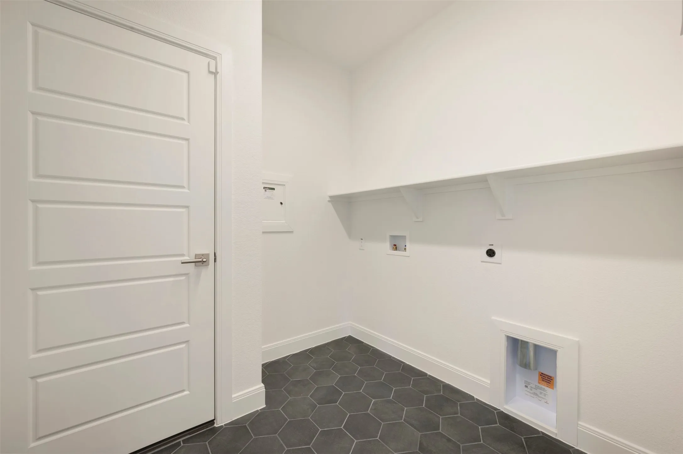 Laundry area featuring hexagonal floor tiles, white baseboards, a flat-panel door with brushed nickel hardware, and a built-in white shelving unit
