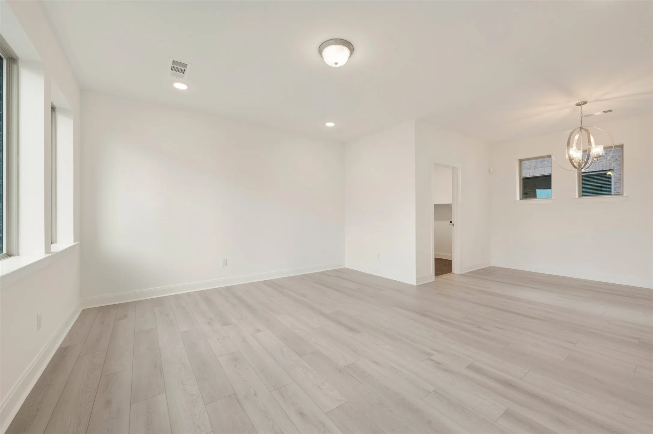 Spacious room featuring light wood-finish flooring, white walls, and multiple windows