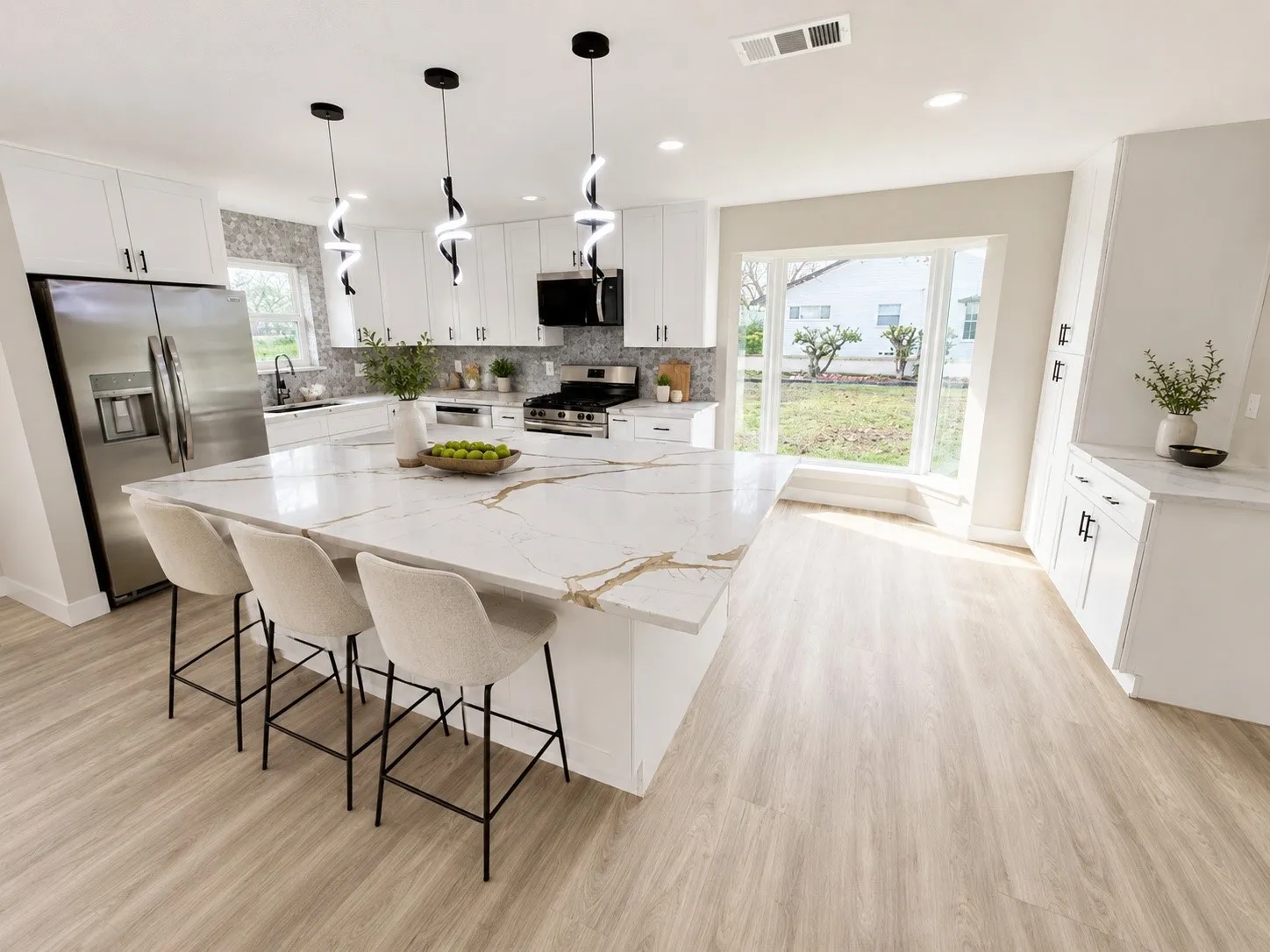 Expansive kitchen featuring a large island with a patterned countertop, white cabinetry, integrated stainless steel appliances, modern pendant lighting, and wood-finish flooring