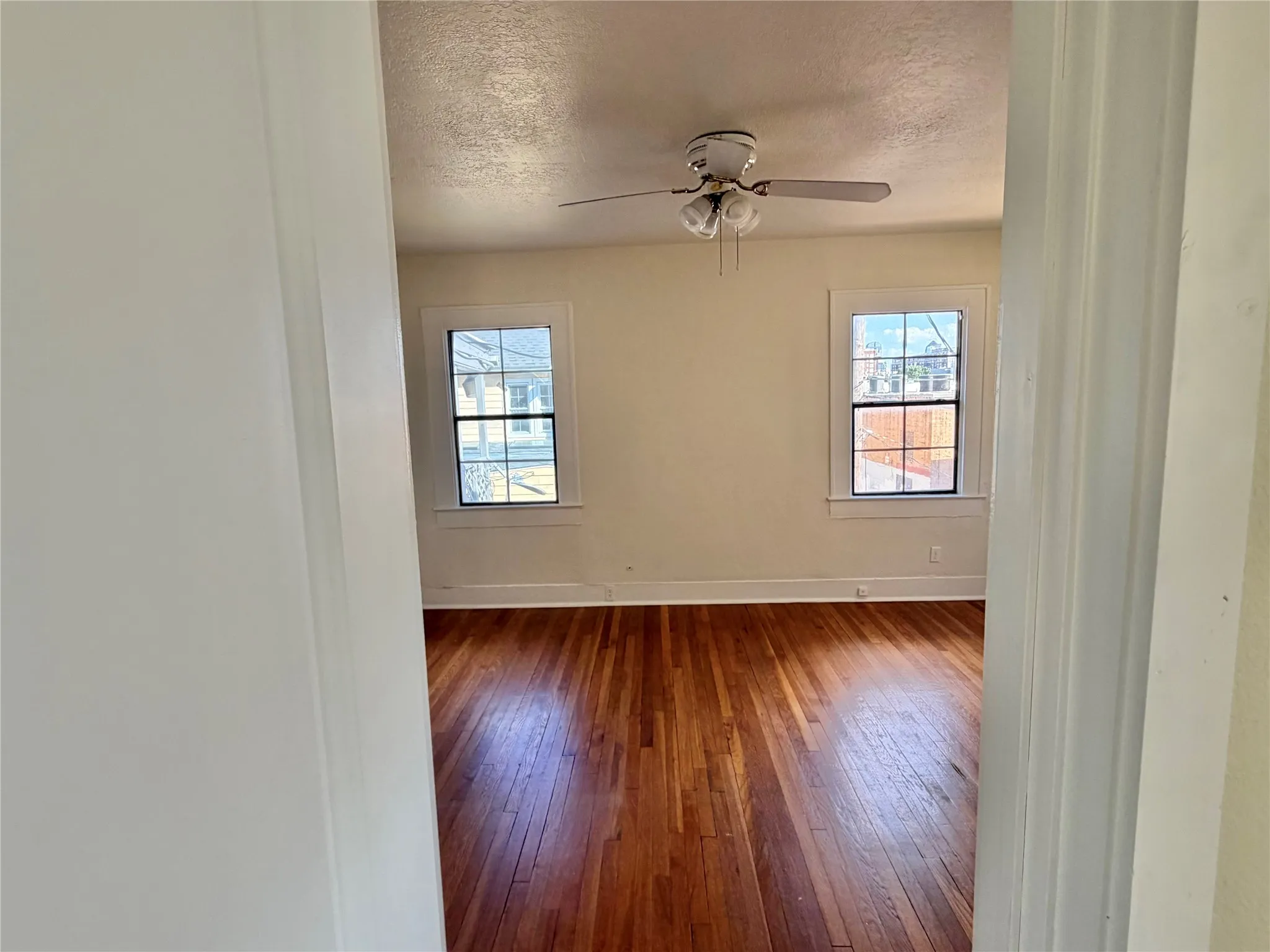 Hardwood flooring, dual windows with white trim, and a ceiling fan with integrated lighting