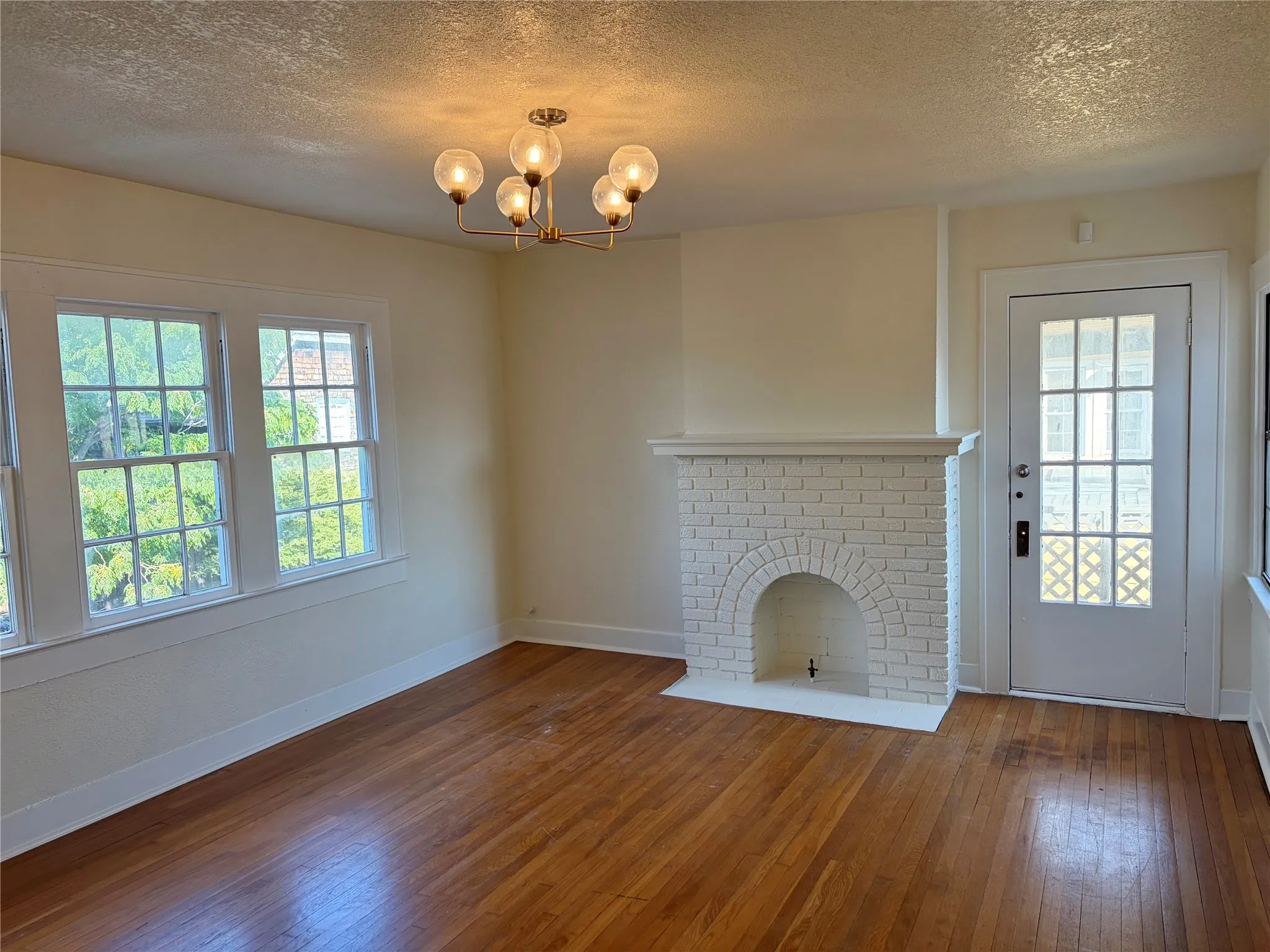 Hardwood flooring throughout, white brick fireplace, multiple pane windows, glass-paned door, and a six-light chandelier
