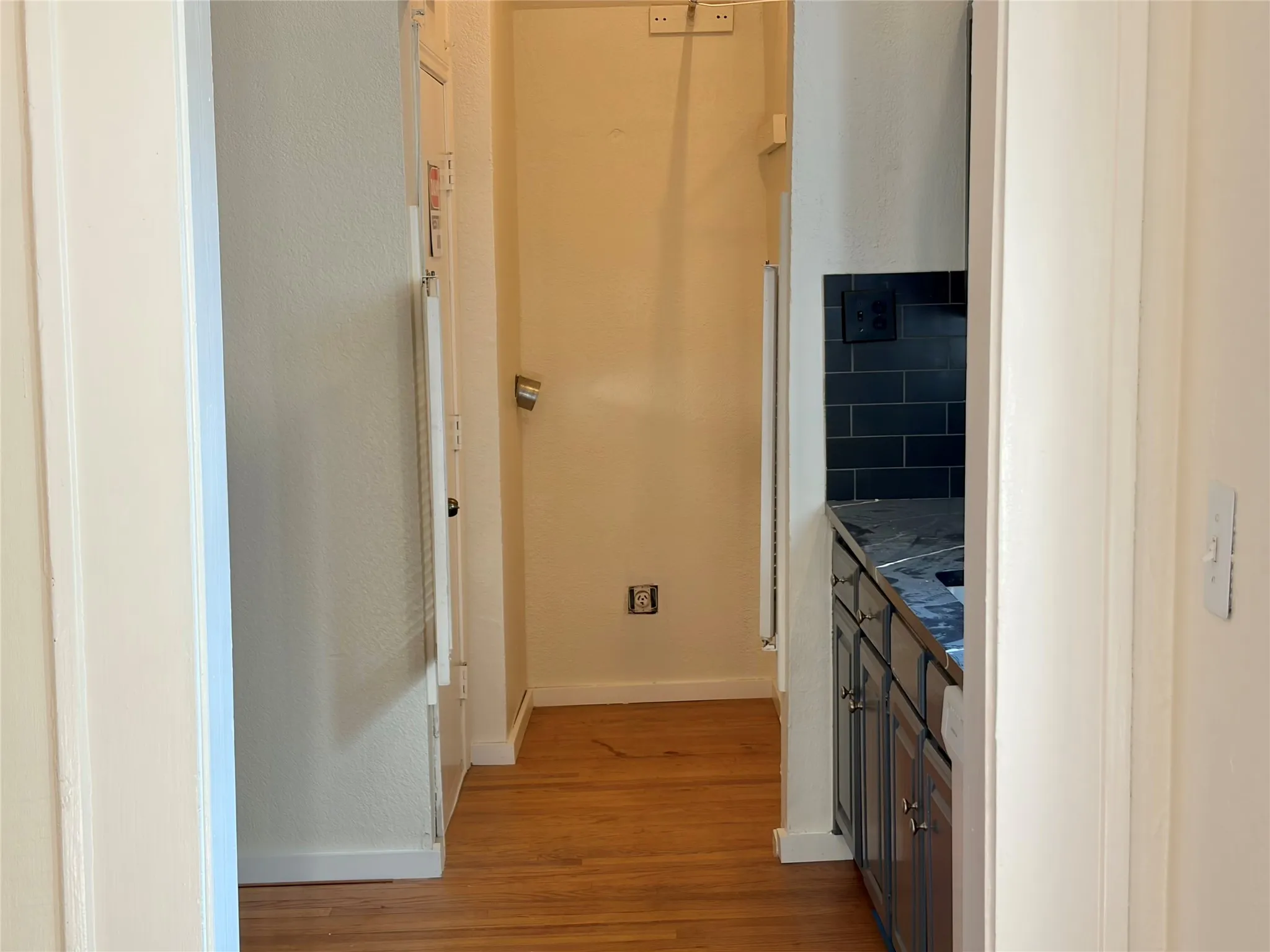 Wood-finish flooring throughout, dark subway tile backsplash, and dark shaker-style cabinetry with metal hardware