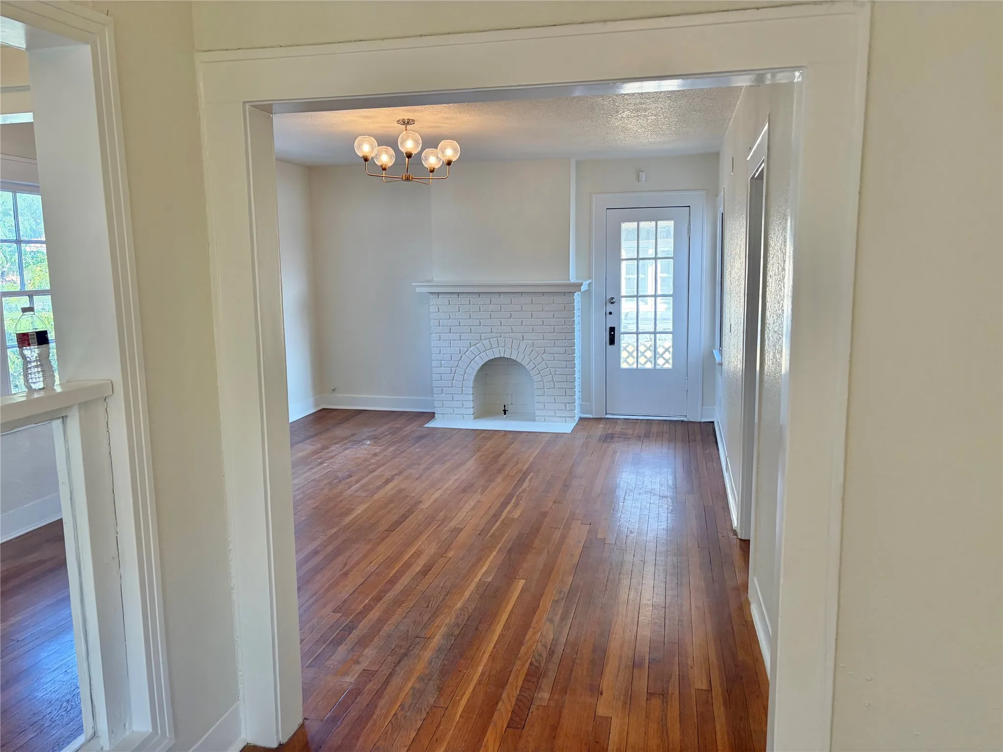 Hardwood flooring throughout, a white brick fireplace, and a decorative ceiling light fixture