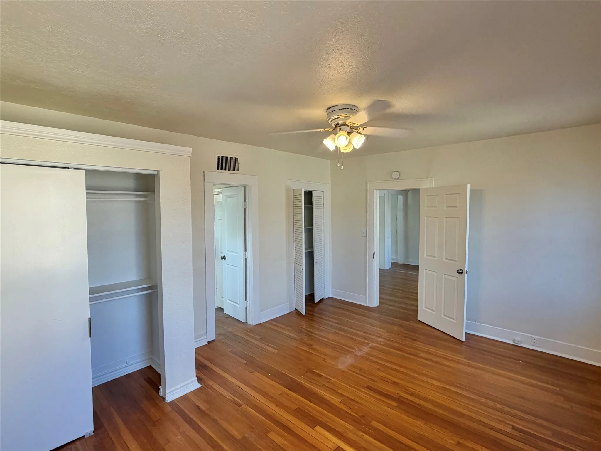 Hardwood flooring, ceiling fan with integrated lighting, multiple doorways, and a built-in closet with sliding doors