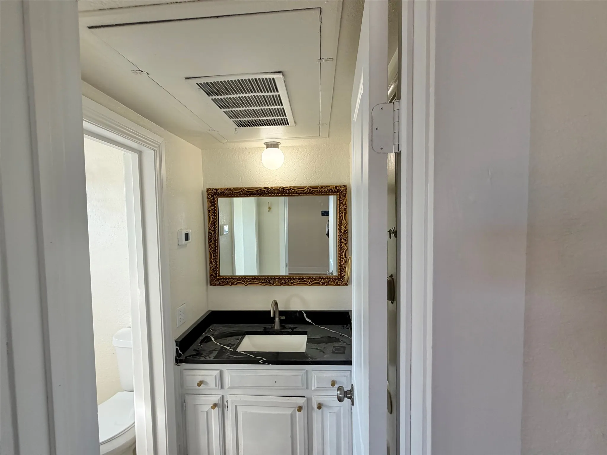 White vanity cabinetry with gold-finish hardware, black countertop, and undermount sink with a chrome-finish faucet
