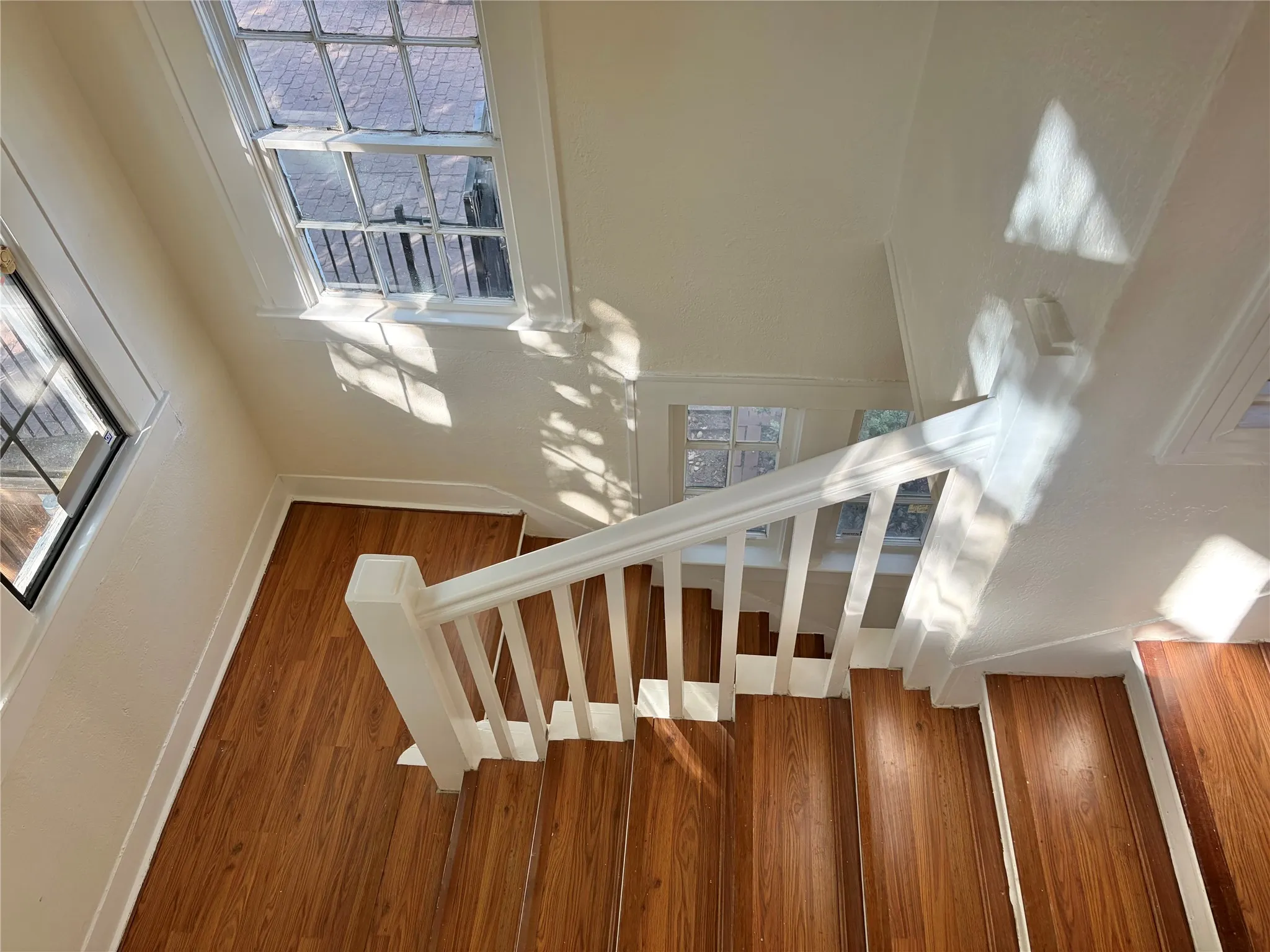 Wood-finish flooring on stairs, white painted balusters and handrail, multiple paneled windows, and light-toned wall finishes