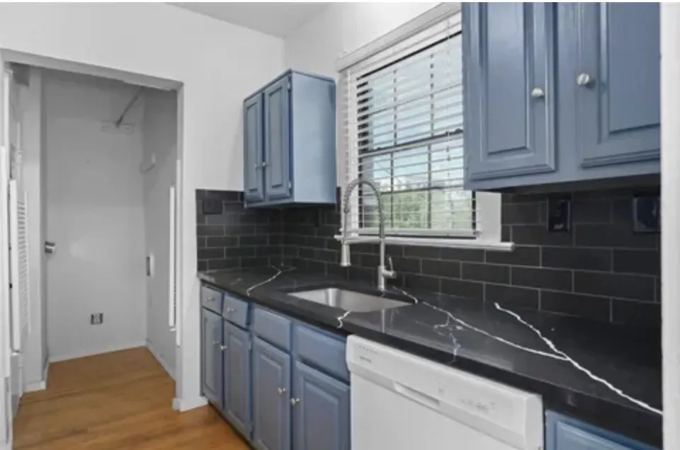 Kitchen featuring blue cabinetry, dark countertops with white veining, a stainless steel sink with a gooseneck faucet, and a subway tile backsplash