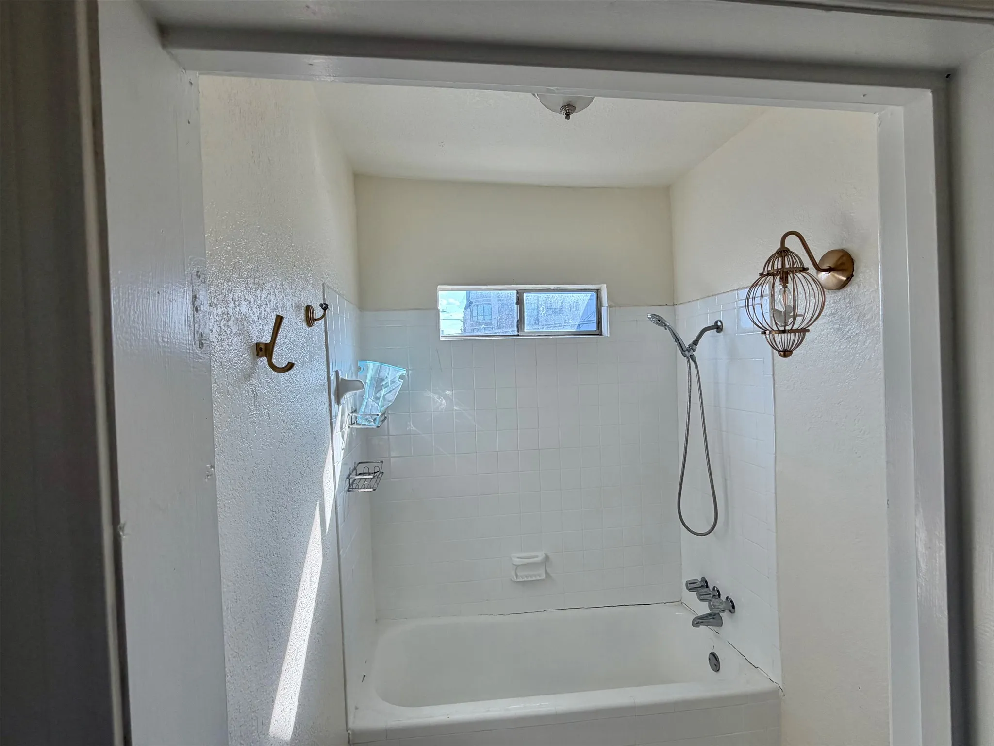 White tiled bath enclosure featuring an integrated tub, shower, and small window