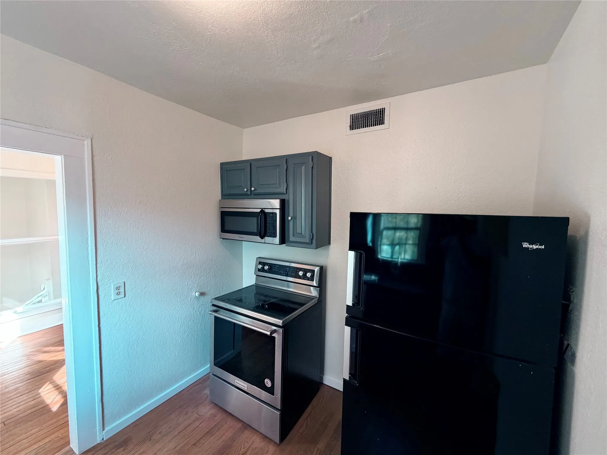 Wood-finish flooring with painted cabinets, stainless steel microwave, electric range, and a black refrigerator