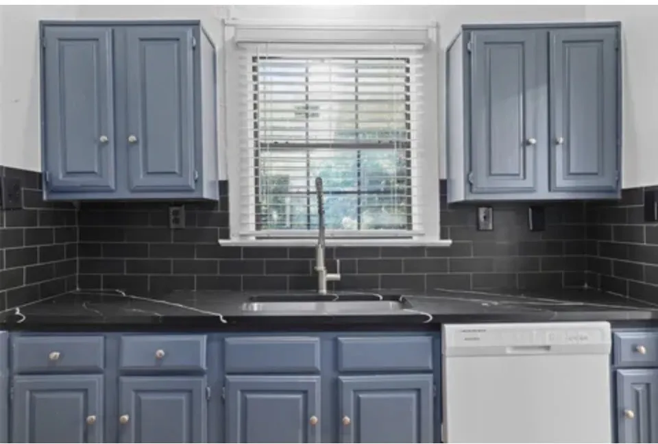 Blue shaker-style cabinetry, black subway tile backsplash, dark countertops, undermount stainless steel sink, and a built-in dishwasher