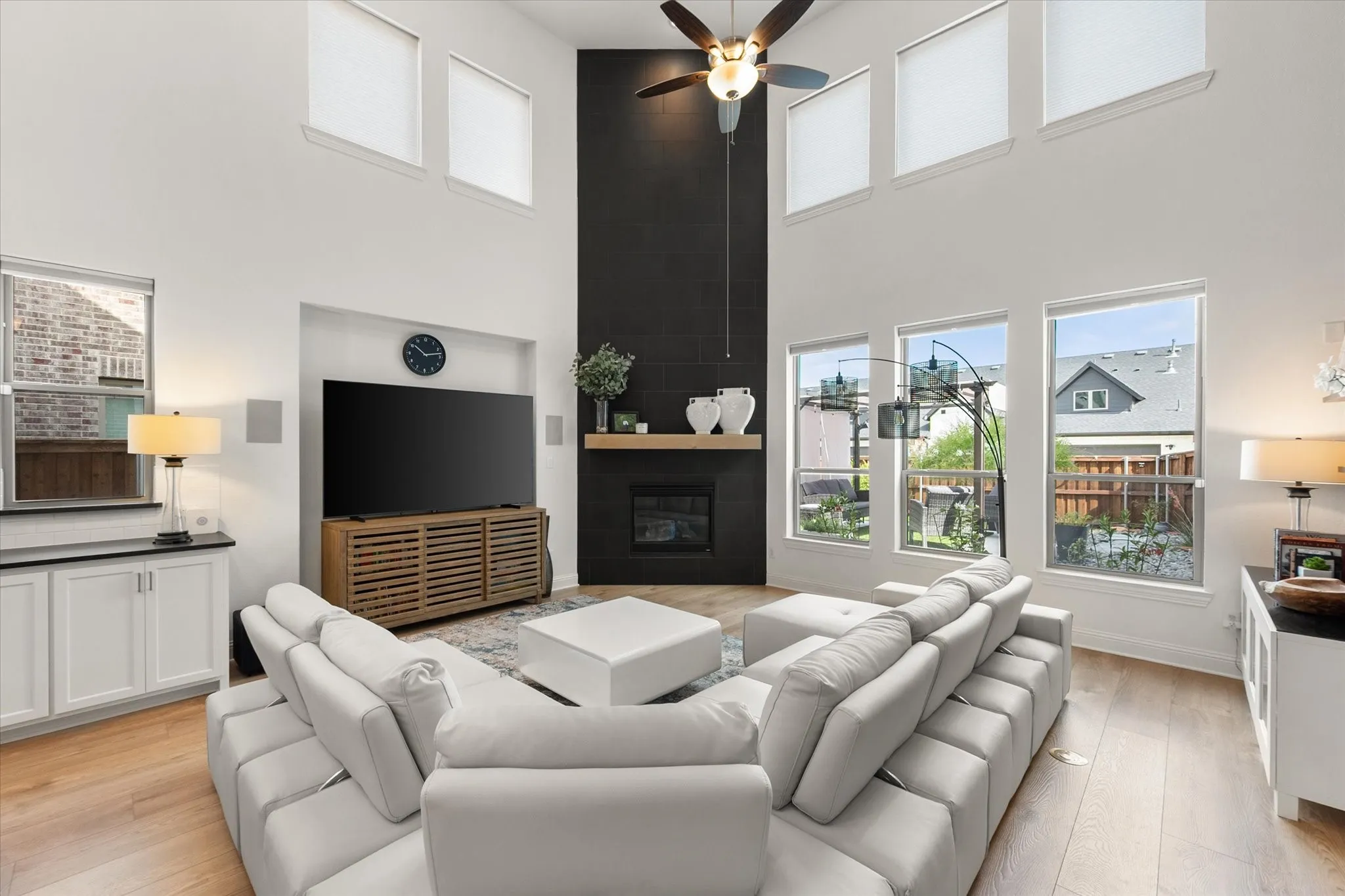 Living area with a large fireplace, a high ceiling, ceiling fan, and light wood-style floors