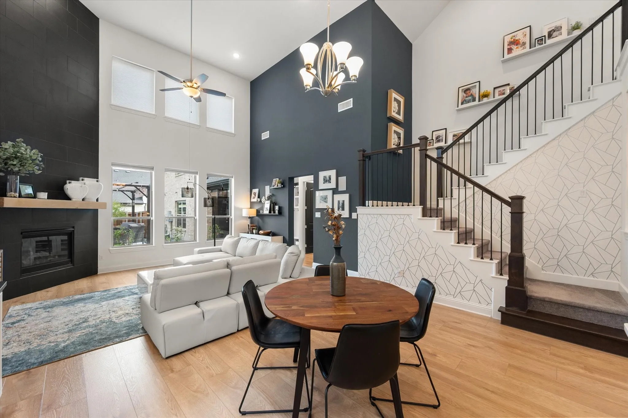 Dining area with high vaulted ceiling, an accent wall, a fireplace, a ceiling fan, and light wood finished floors