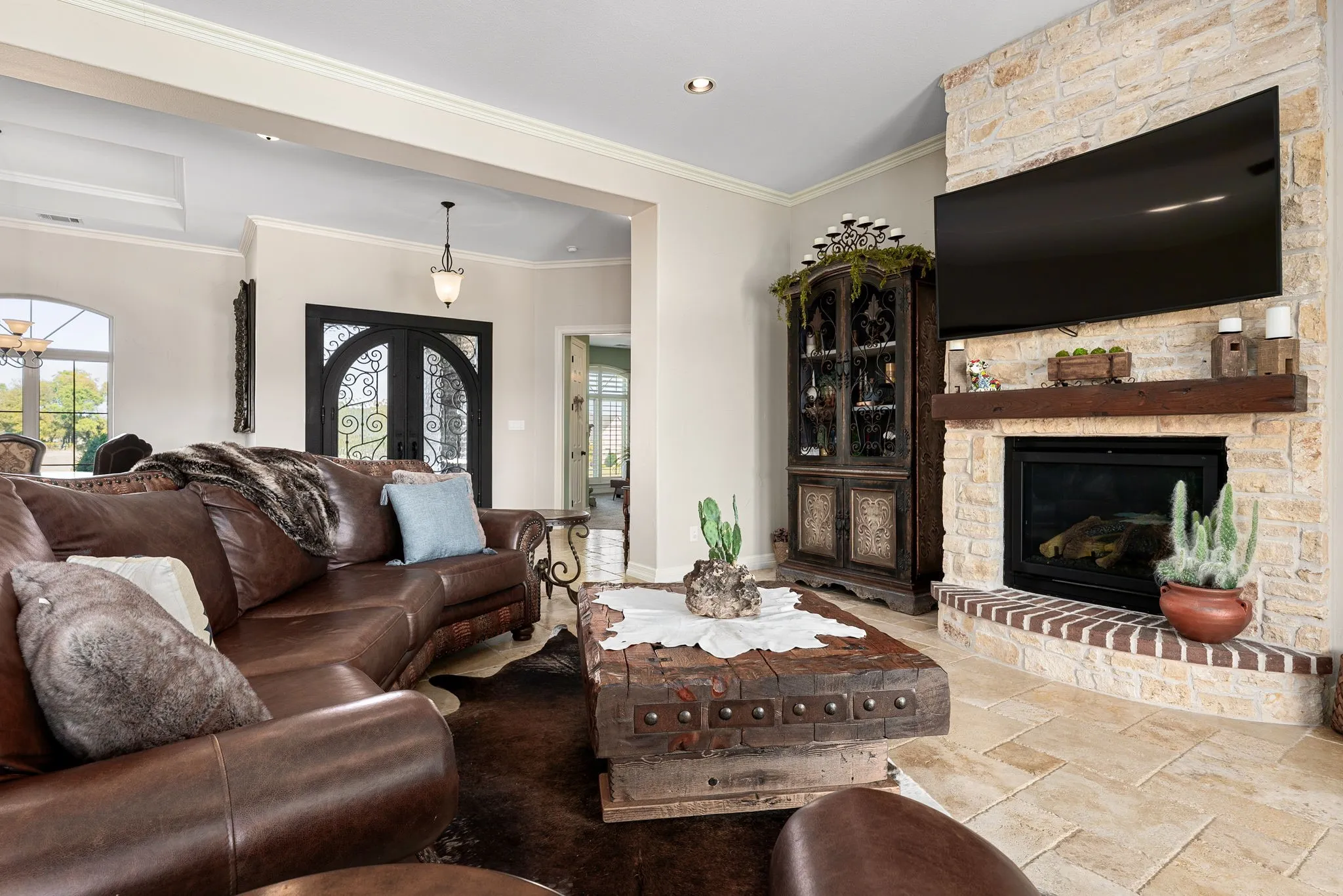 Living room featuring new iron front doors, a stone fireplace, crown molding, stone tile flooring, and recessed lighting