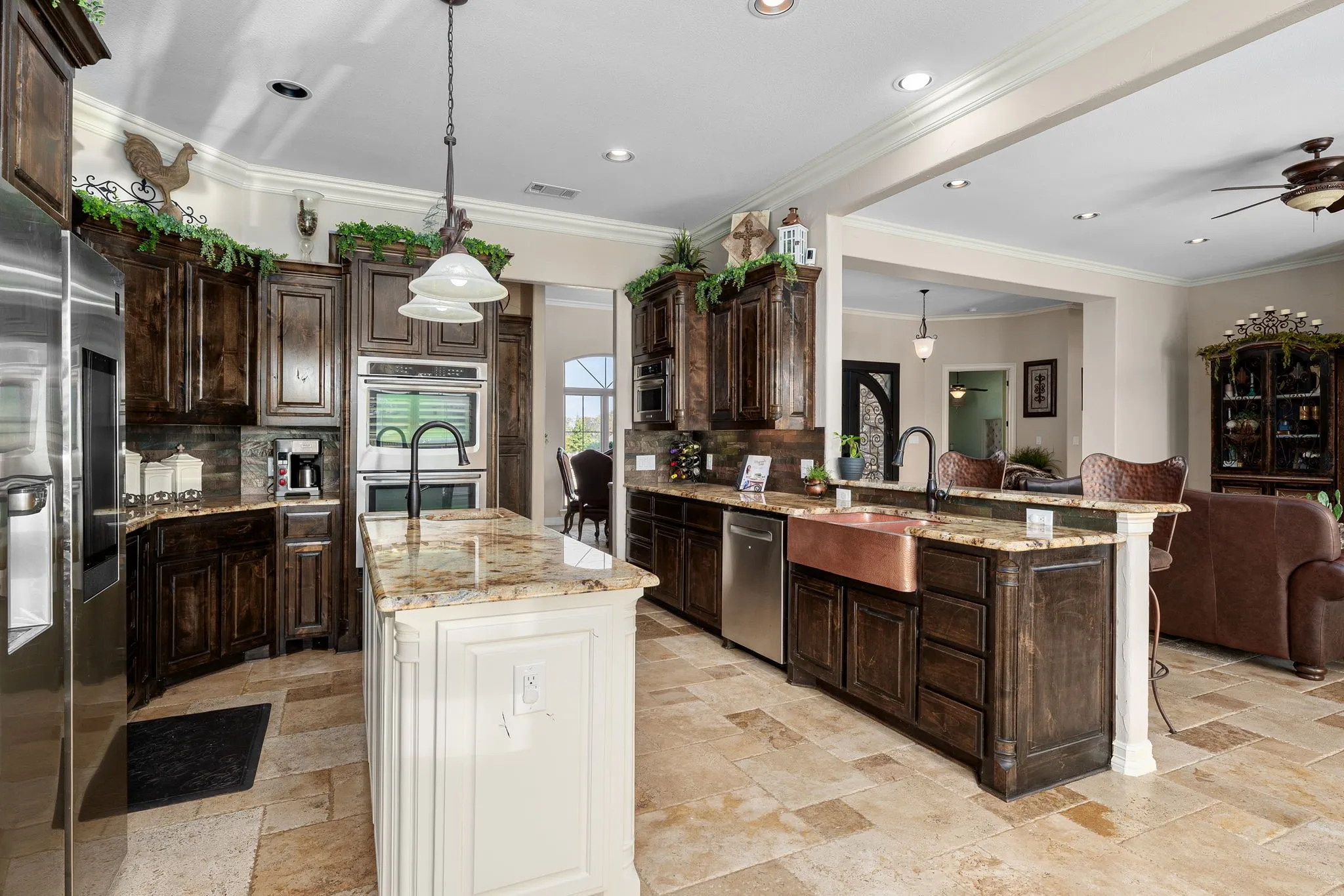 Kitchen featuring dark brown cabinetry, granite countertops, appliances with stainless steel, cast iron sink, open floor plan, and crown molding