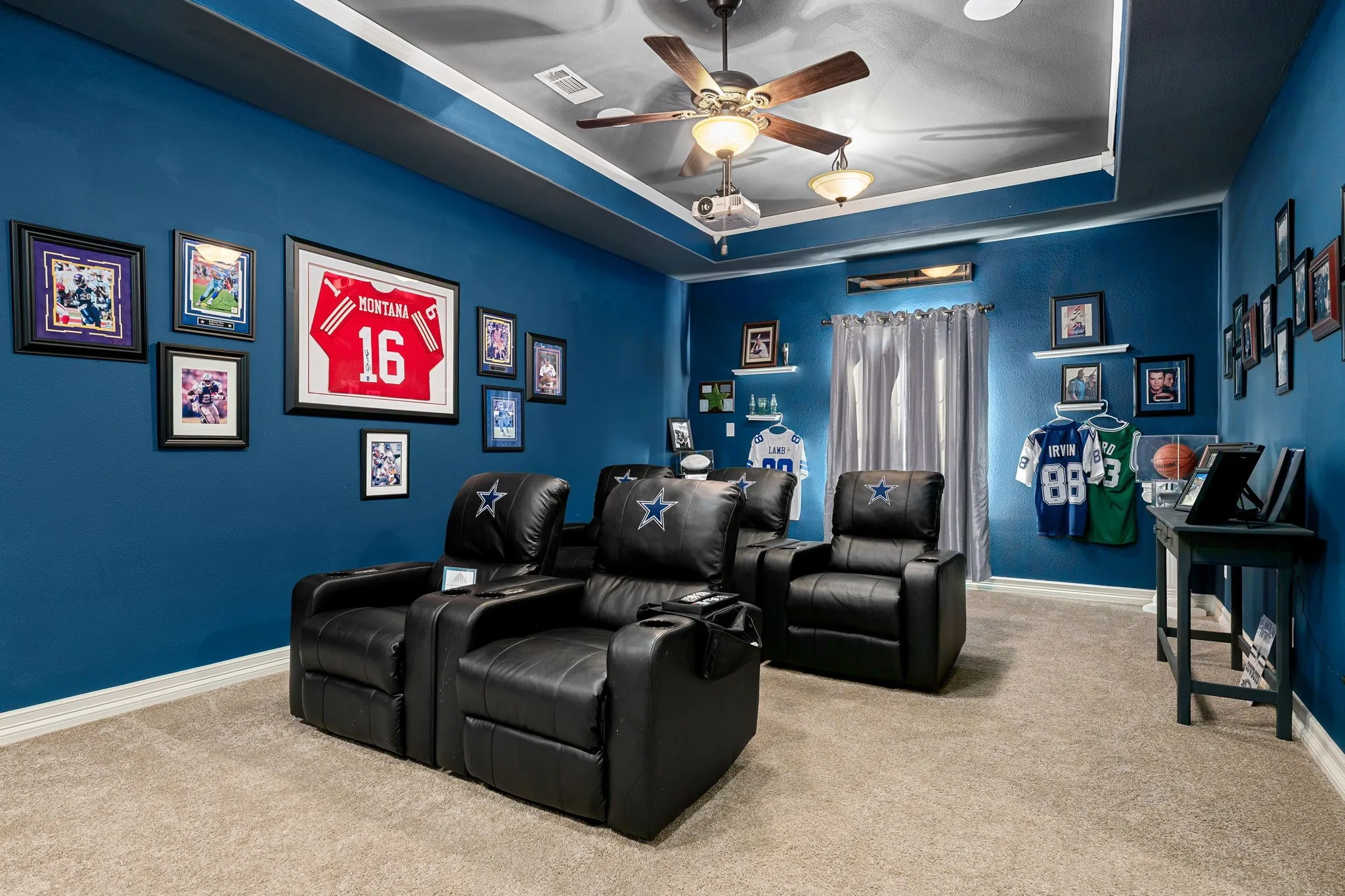 Carpeted home theater room featuring a tray ceiling and a ceiling fan