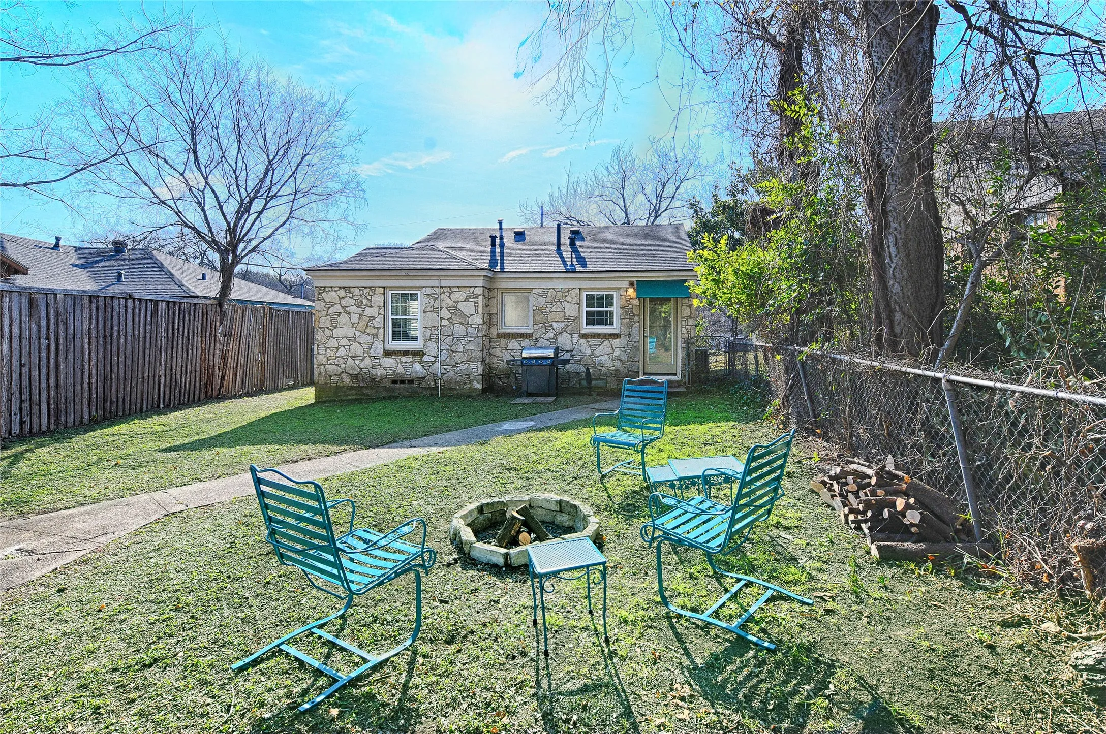 Back of property with stone siding, a fenced backyard, and a fire pit