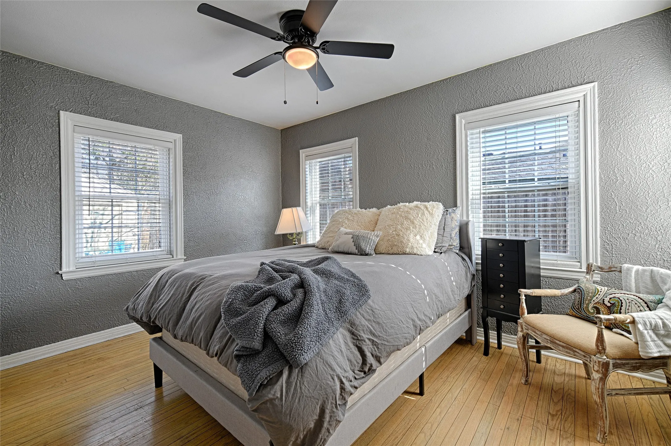 Bedroom with a textured wall, tons of natural light, light wood flooring, and ceiling fan