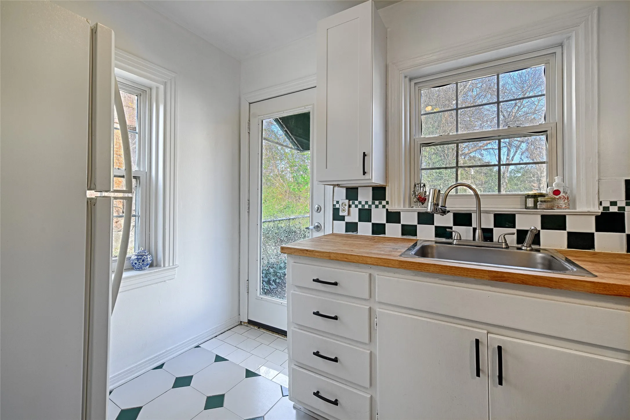 Kitchen with freestanding refrigerator, white cabinetry, tasteful backsplash, and plenty of natural light