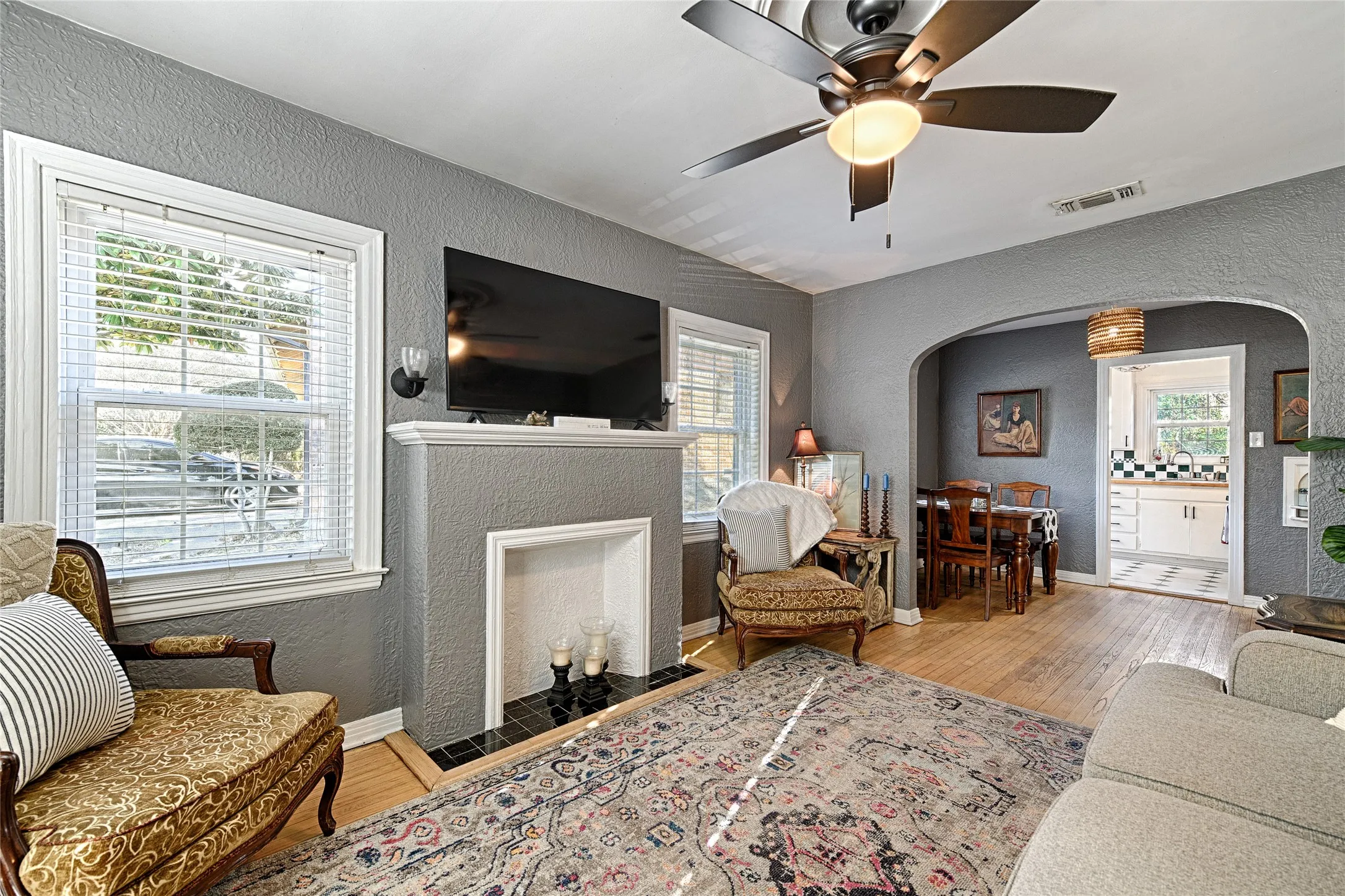 Living area with a textured wall, light wood-style floors, a fireplace with flush hearth, arched walkways, and ceiling fan