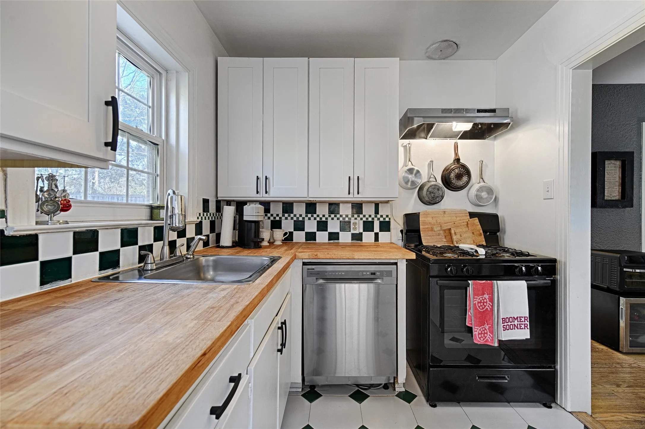 Kitchen with white cabinetry, black gas range oven, dishwasher, and range hood