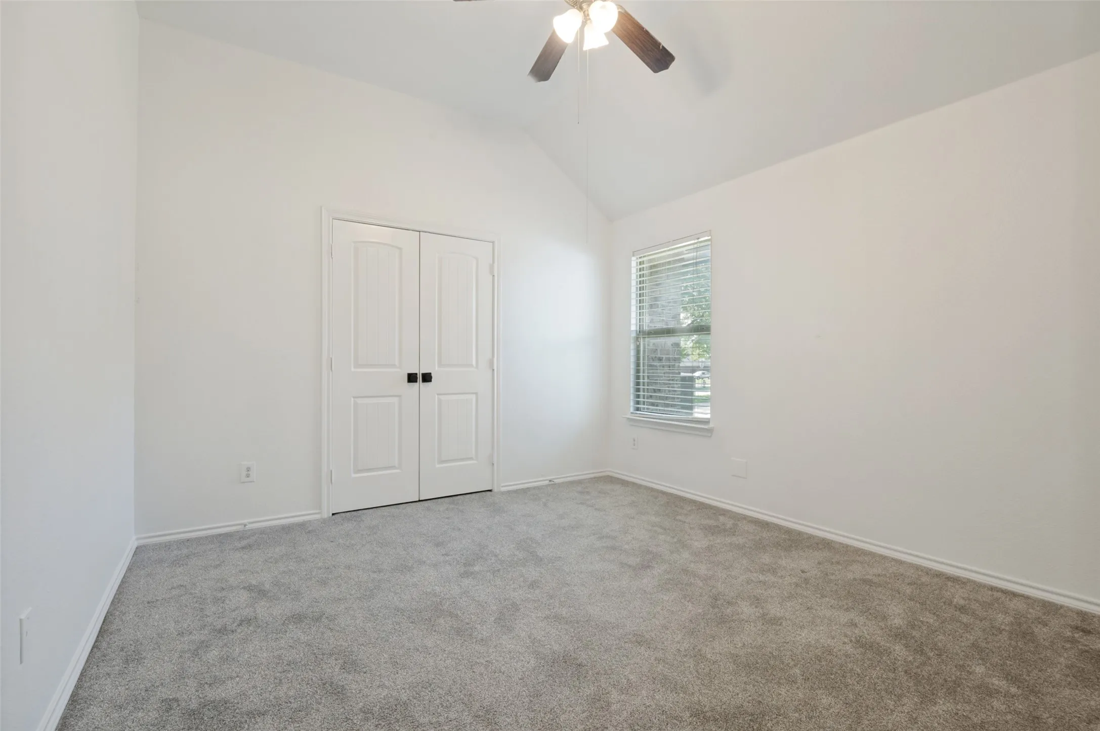 Spacious room featuring vaulted ceilings, light gray carpeting, and a ceiling fan with integrated lighting