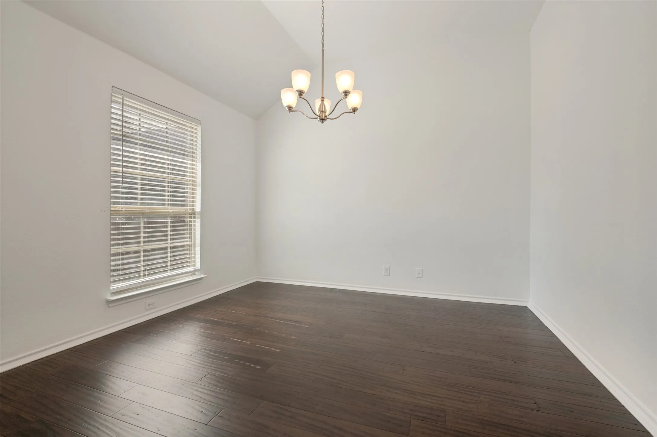 Vaulted ceiling room featuring wood-finish flooring, a chandelier with frosted glass shades, and a large window with horizontal blinds