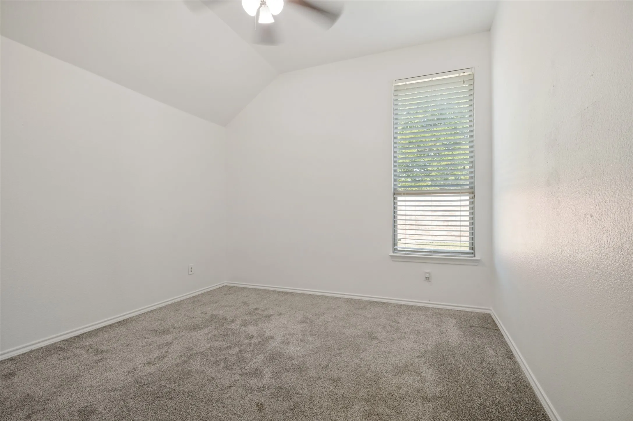 Bright interior space featuring a tall window with horizontal blinds, sloped ceiling, and a ceiling fan with integrated lighting