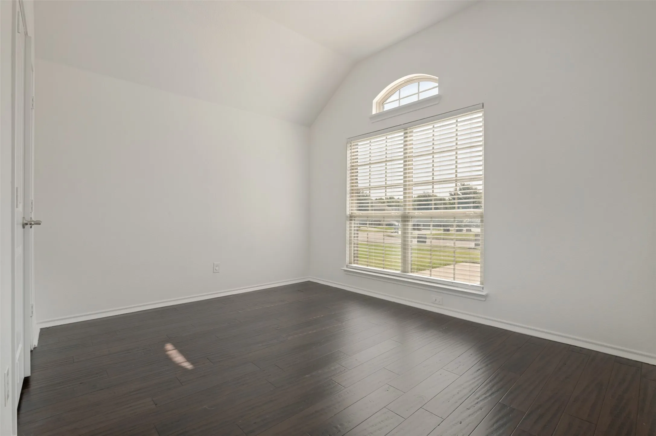 Vaulted ceiling room featuring a large window with blinds and an arched transom window