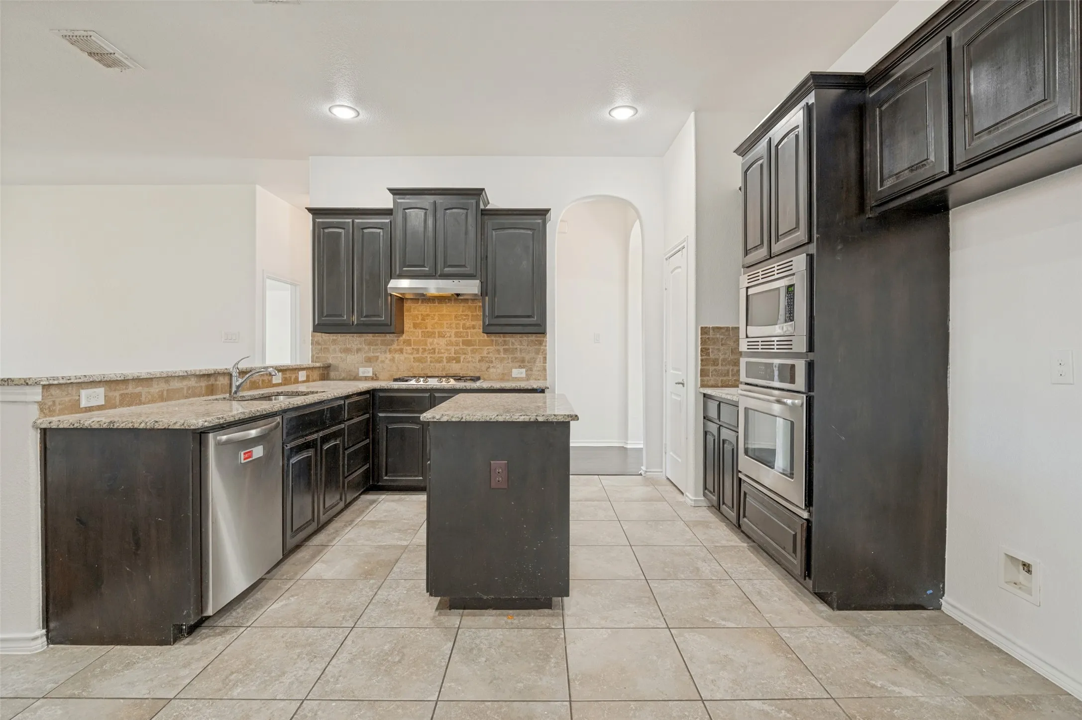 Kitchen featuring dark wood cabinetry, light-toned tile flooring, and granite countertops