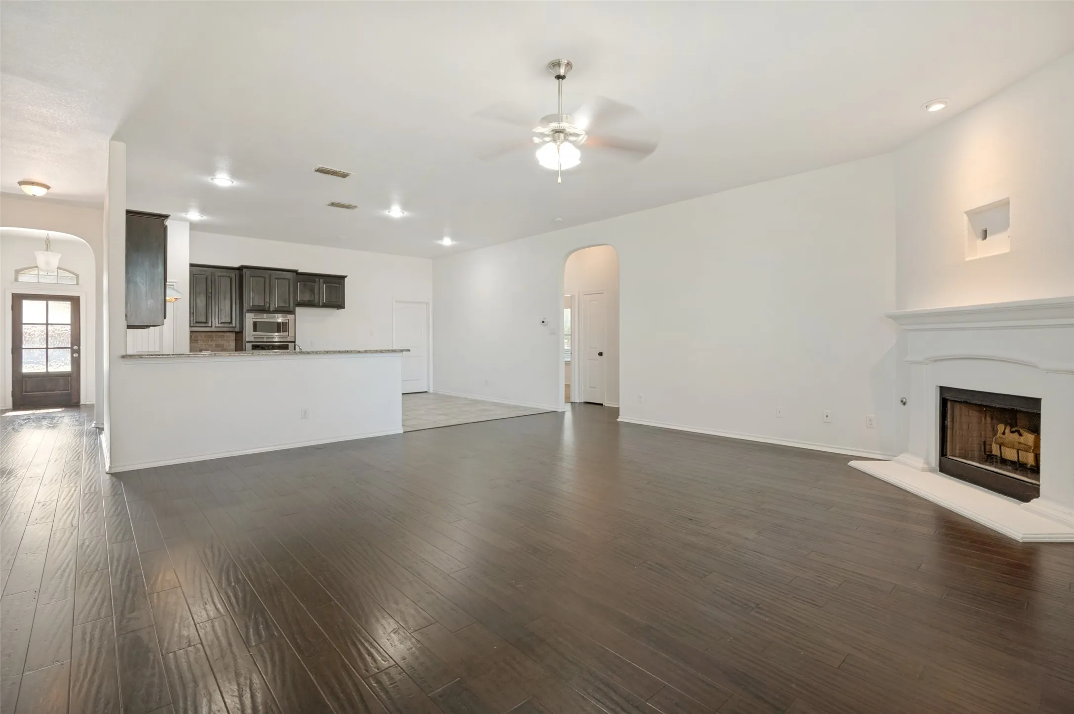 Expansive living area featuring wood-finish flooring, a white mantel fireplace, and a ceiling fan