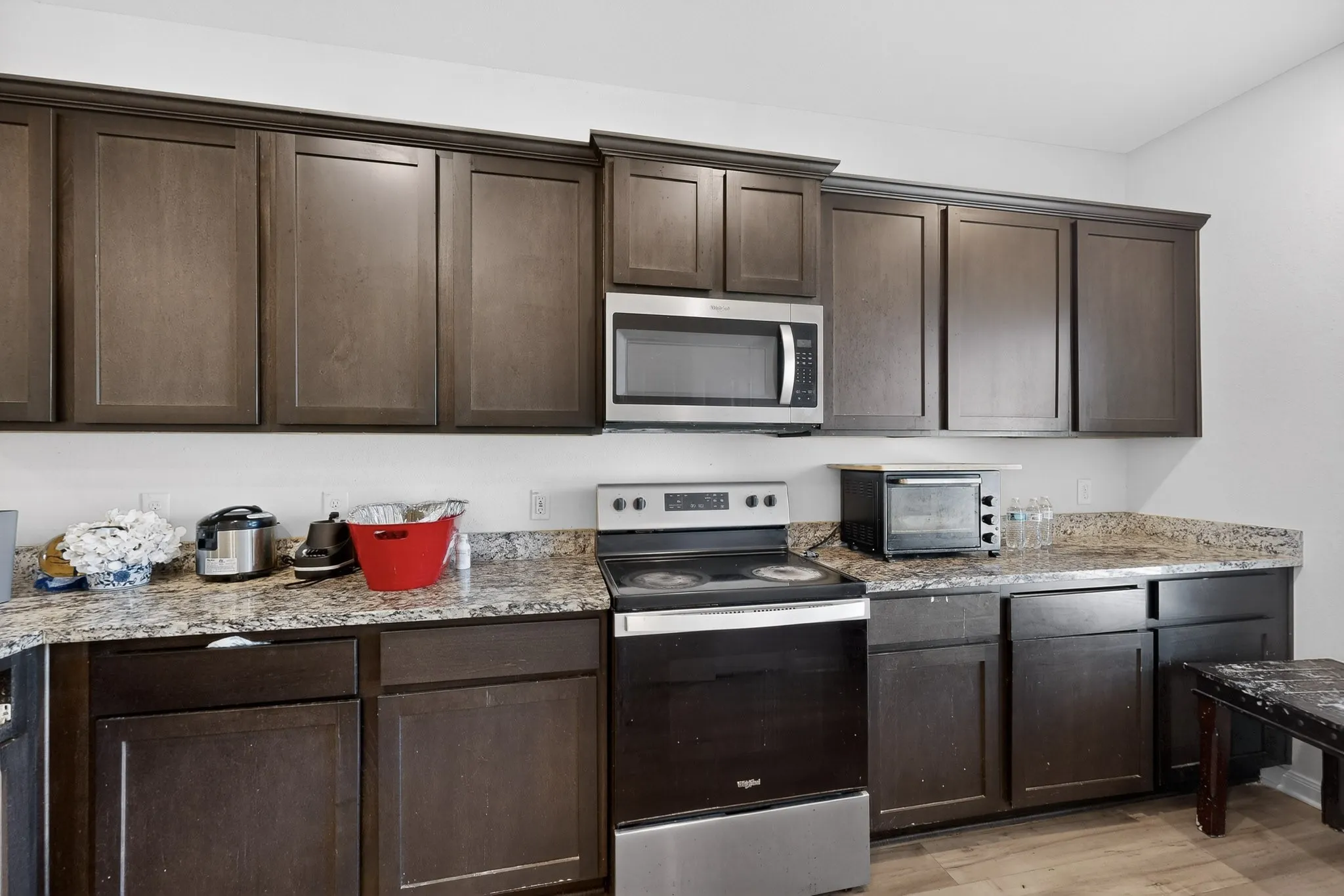 Kitchen featuring stainless steel appliances, dark brown cabinetry, light stone countertops, and light wood finished floors