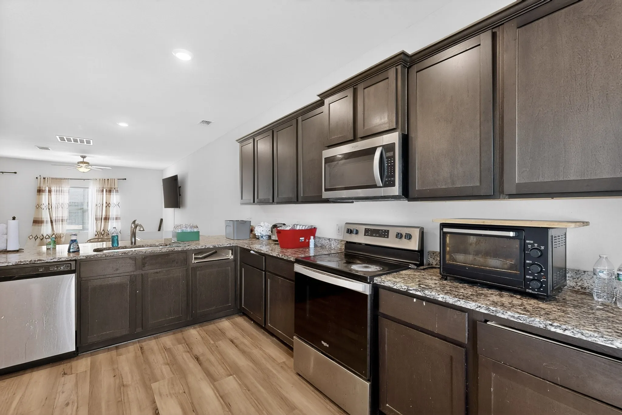 Kitchen featuring dark brown cabinets, appliances with stainless steel finishes, light stone countertops, light wood finished floors, and recessed lighting