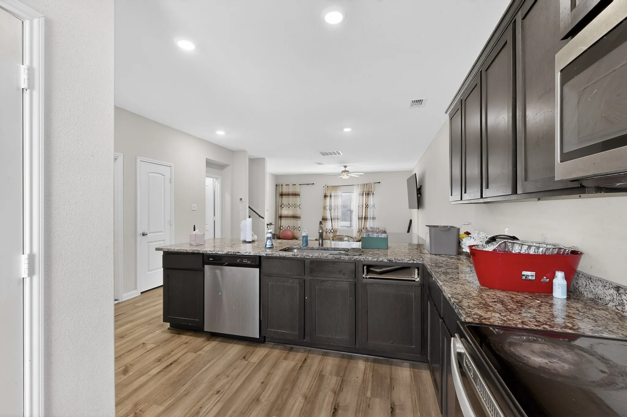 Kitchen with appliances with stainless steel finishes, dark stone counters, a peninsula, light wood finished floors, and dark brown cabinetry