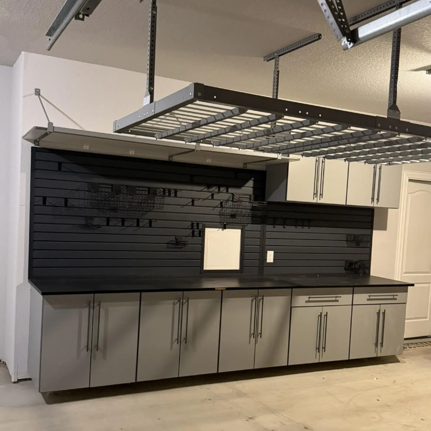 Integrated garage storage solution featuring expansive cabinetry, a dark countertop, and a black slatwall system
