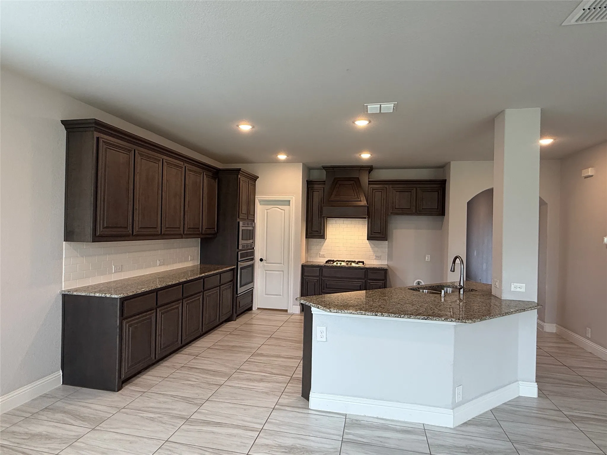 Spacious kitchen featuring dark wood cabinetry, granite countertops, an undermount sink, a built-in oven and microwave, and a tile backsplash
