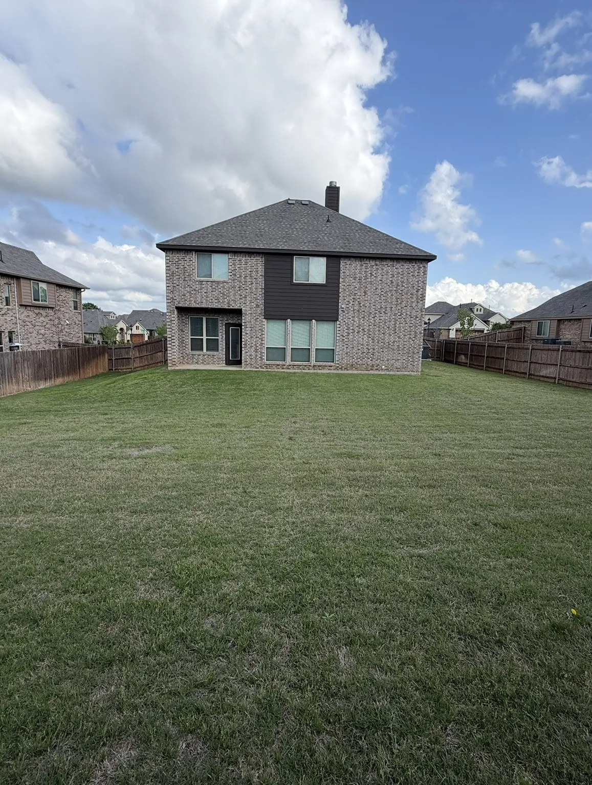 Expansive backyard featuring a manicured lawn, full privacy fencing, and a two-story brick exterior with dark siding accents