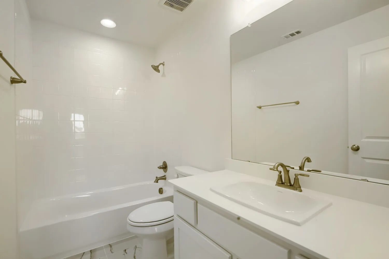 Bathroom featuring a white vanity with integrated sink, a large wall-mounted mirror, brushed bronze fixtures, and white subway tile surround in the tub and shower area