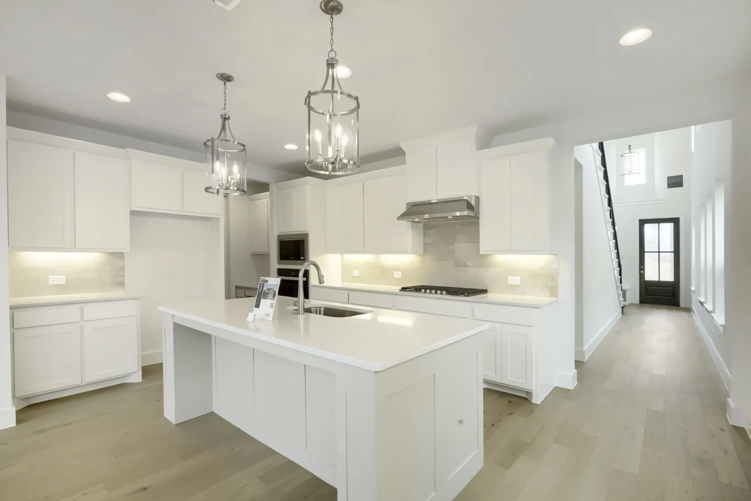 Modern kitchen featuring white cabinetry, light-toned wood-finish flooring, and a central island with a sink