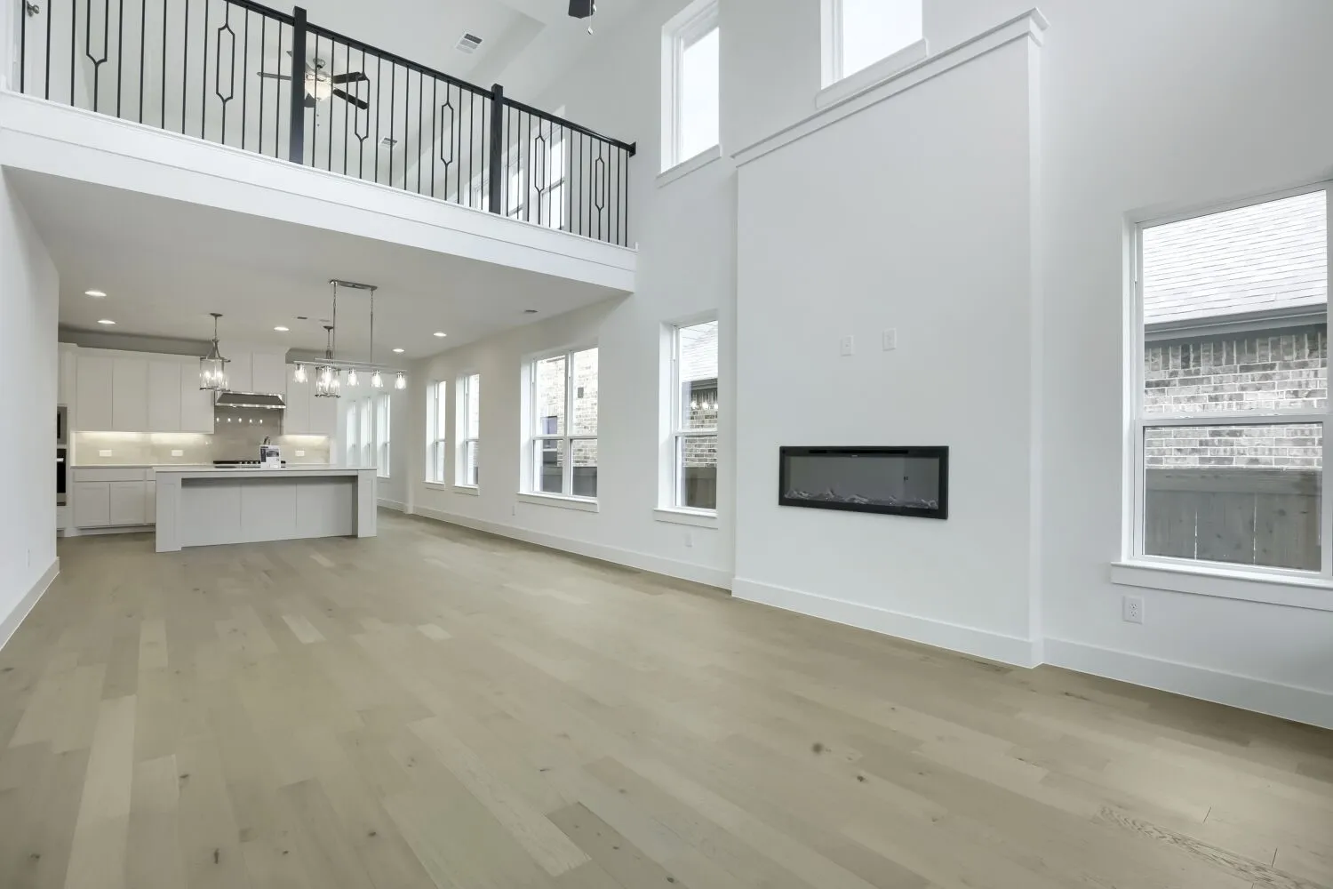 Open-concept living area with high ceilings, light wood-finish flooring, and multiple windows
