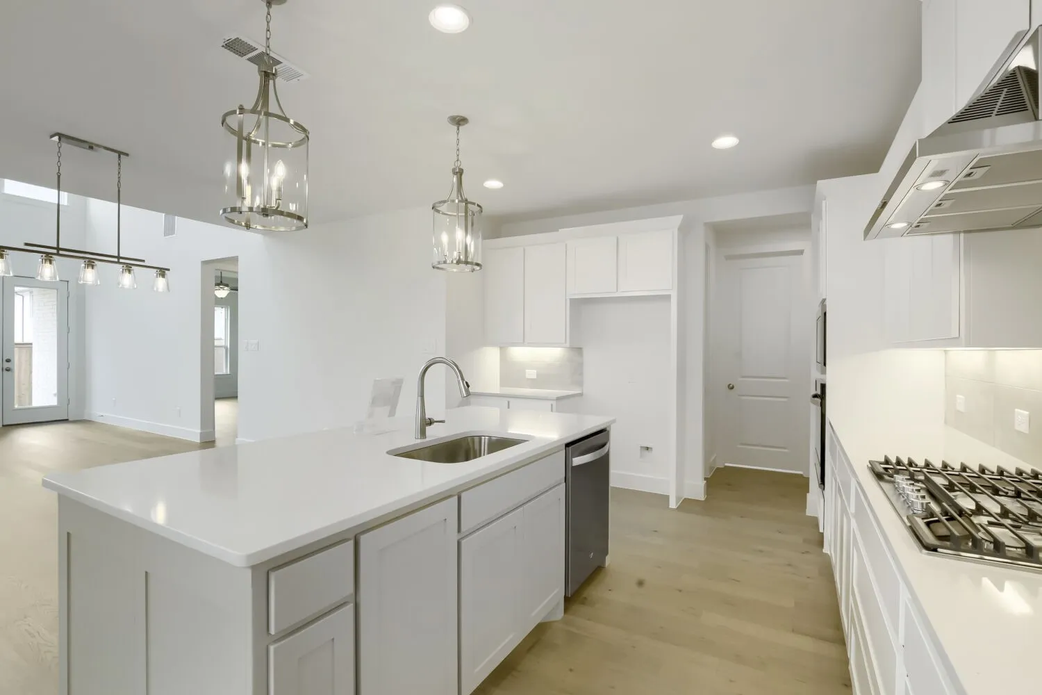 Bright kitchen featuring a central island with an undermount sink, white cabinetry, integrated stainless steel appliances, and wood-finish flooring