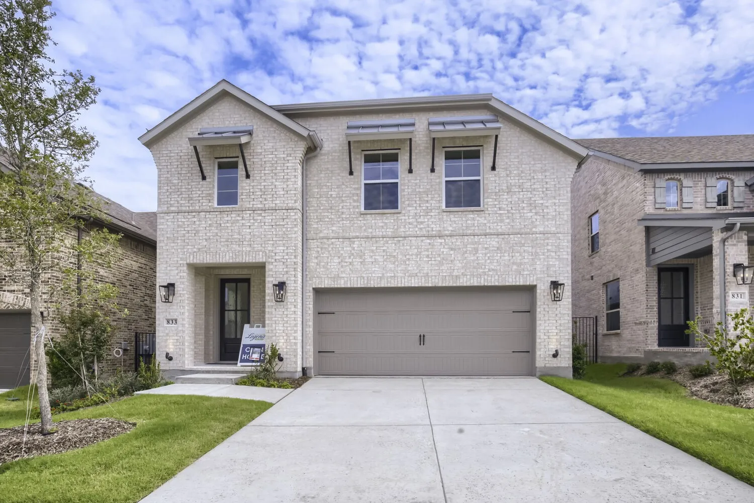 Two-story brick facade residence featuring a two-car garage, covered entry, and decorative window awnings