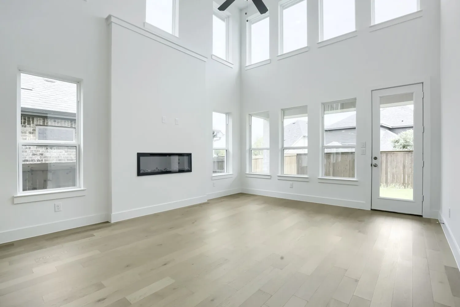 Spacious living area featuring a double-height ceiling, wood-finish flooring, and a linear electric fireplace