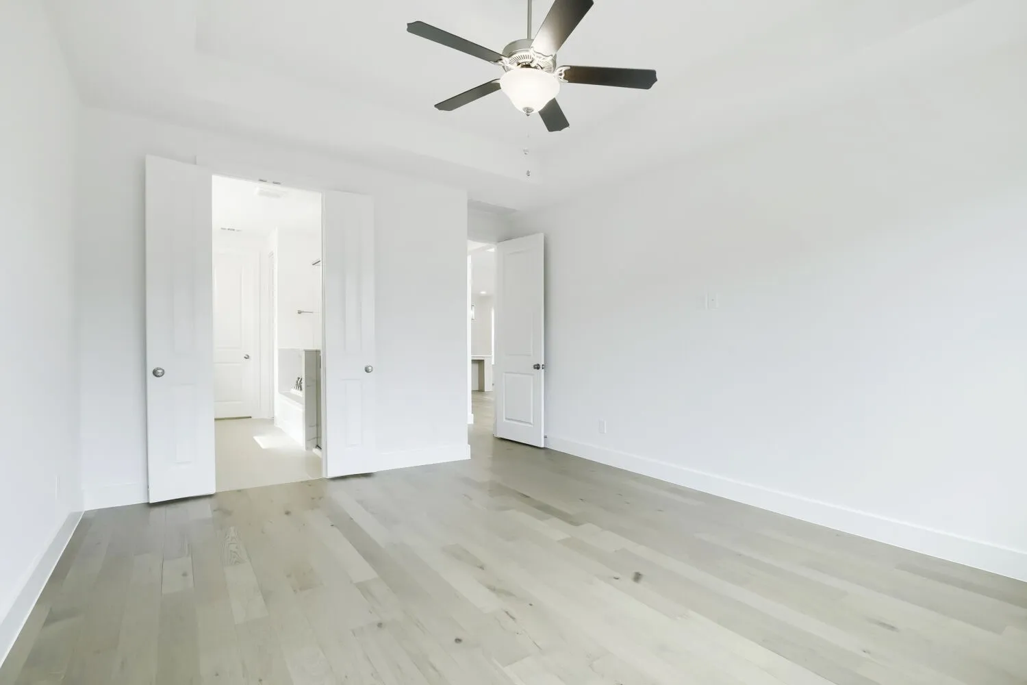 Spacious room featuring light wood-finish flooring, a contemporary ceiling fan with integrated lighting, and a tray ceiling