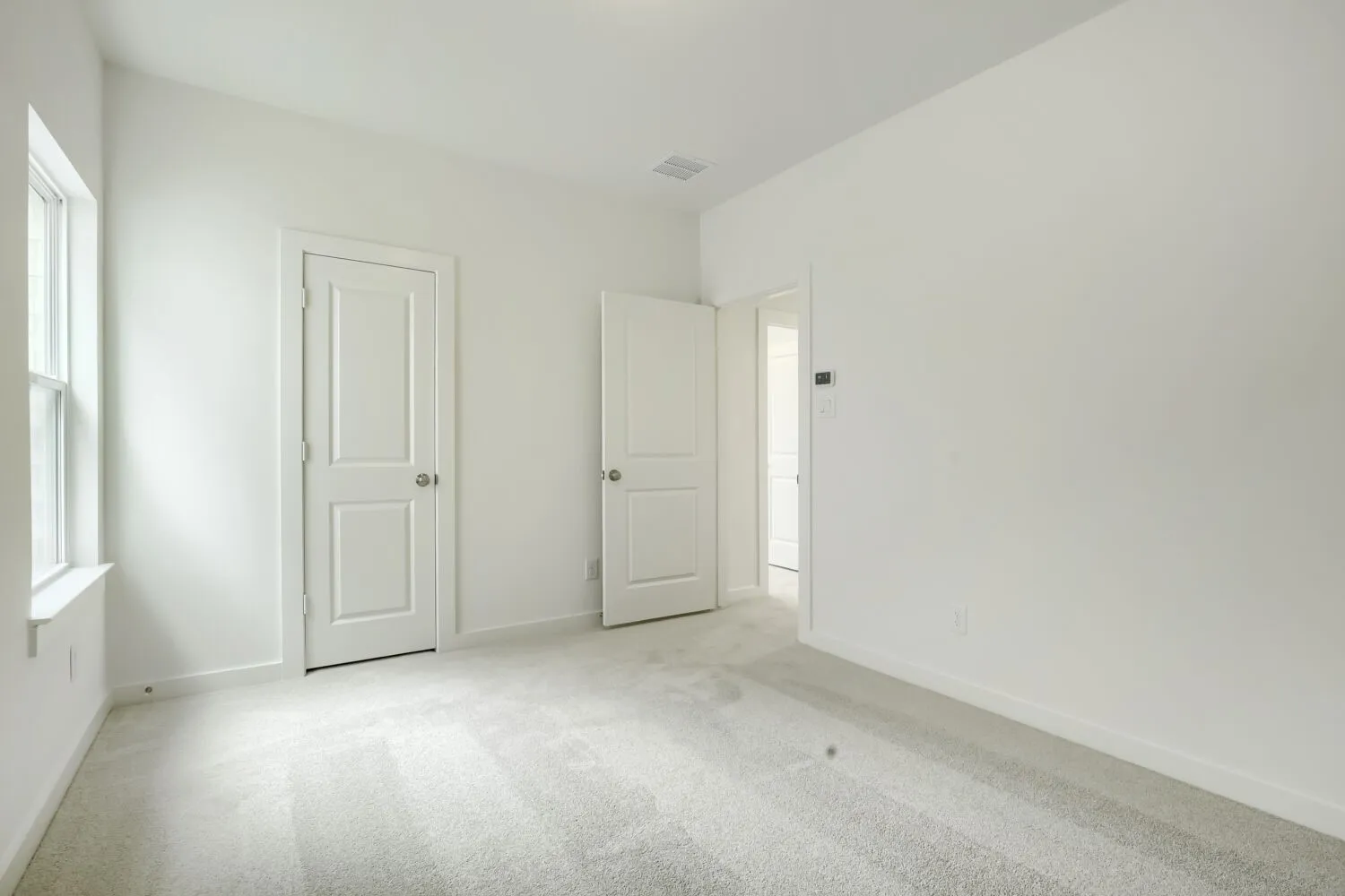Carpeted room with white walls, a single window, and two paneled doors with chrome hardware