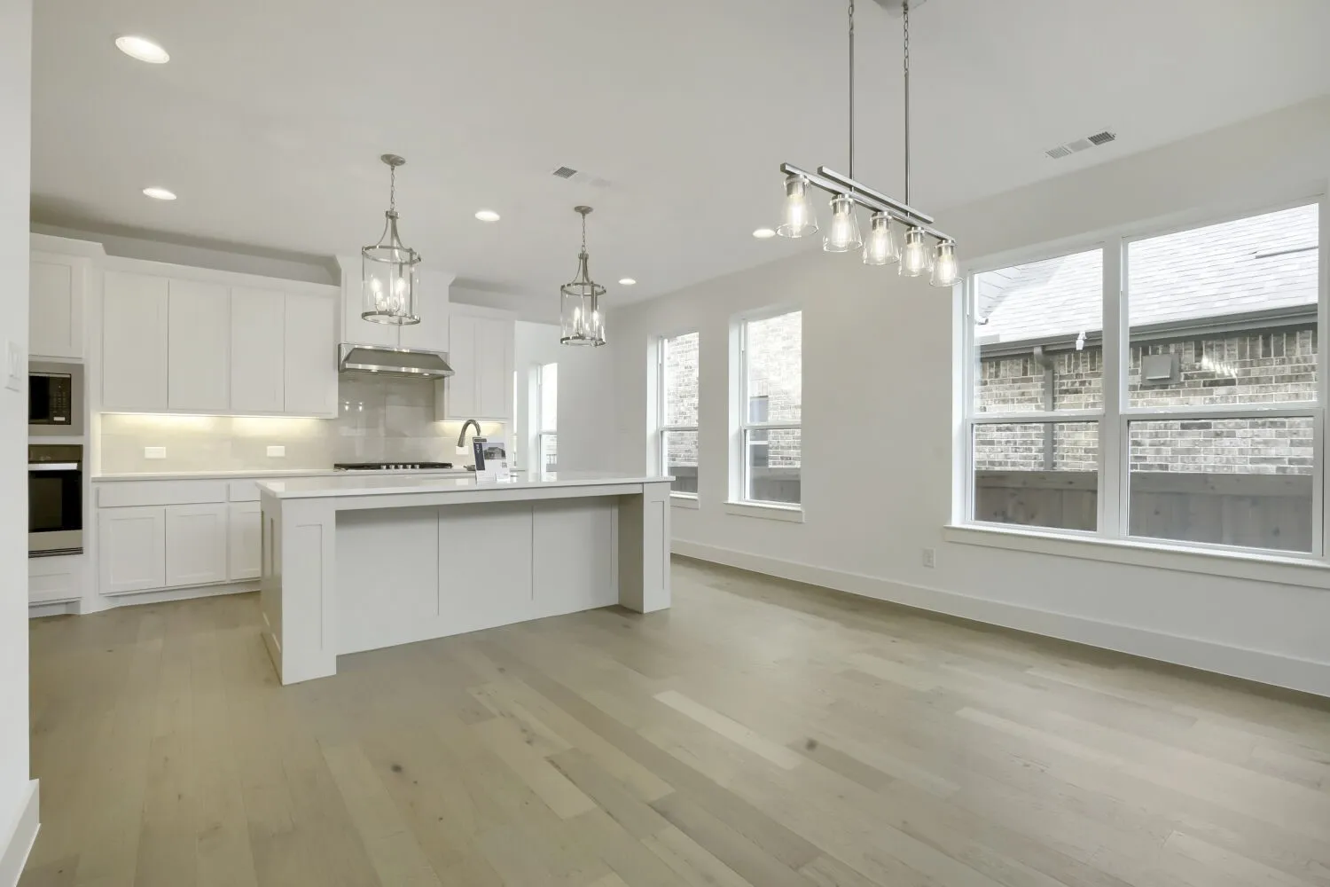 Open-concept kitchen and dining area featuring light wood-finish flooring, white cabinetry, a central island with countertop seating, and multiple windows providing ambient light