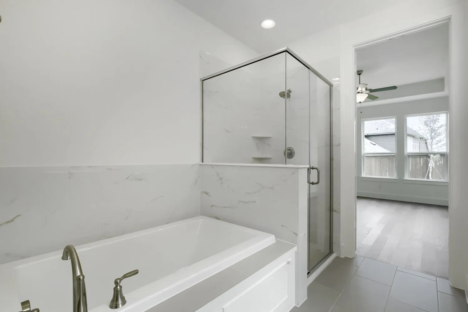 Contemporary bath featuring a built-in tub with brushed nickel fixtures, a frameless glass shower enclosure, and white marble-look tile surround
